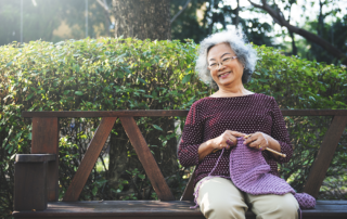 Senior woman sitting on bench outside knitting at memory care community
