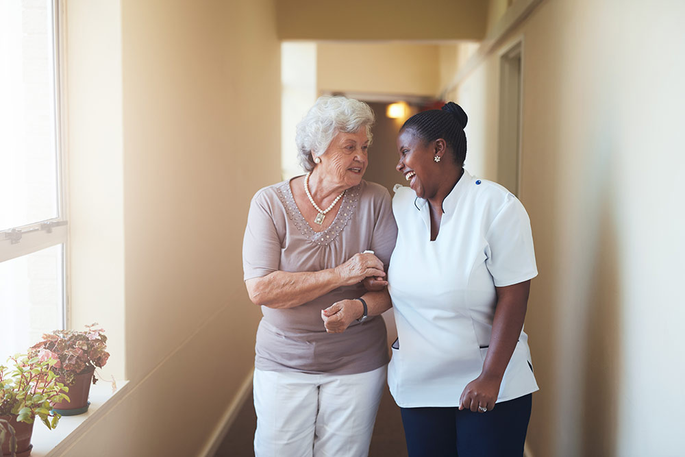 Senior woman walking with caregiver in dementia assisted living facility