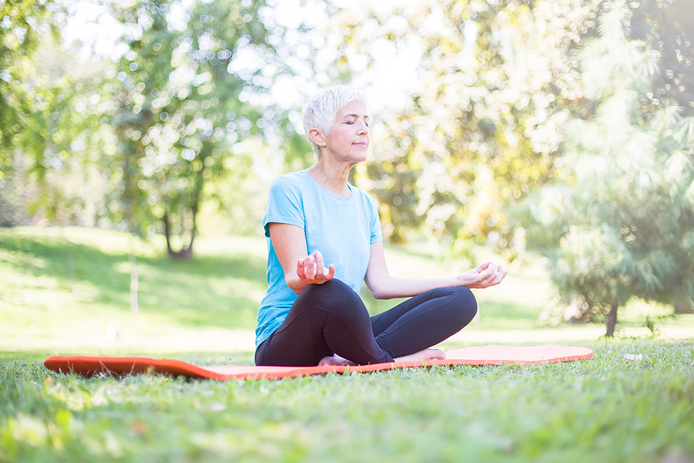 Senior woman meditating outside in grass