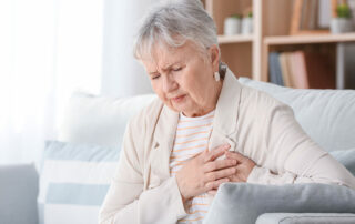 Senior woman sitting on couch, clutching at heart area with worried look