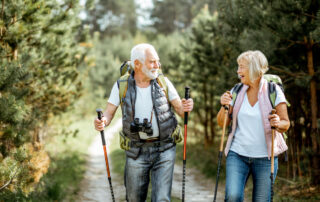 A smiling senior couple on a nature walk with backpacks and walking sticks