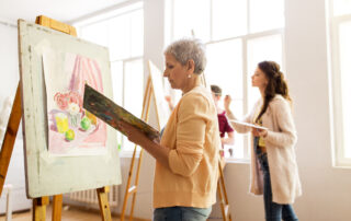 A senior woman painting on a canvas during art class