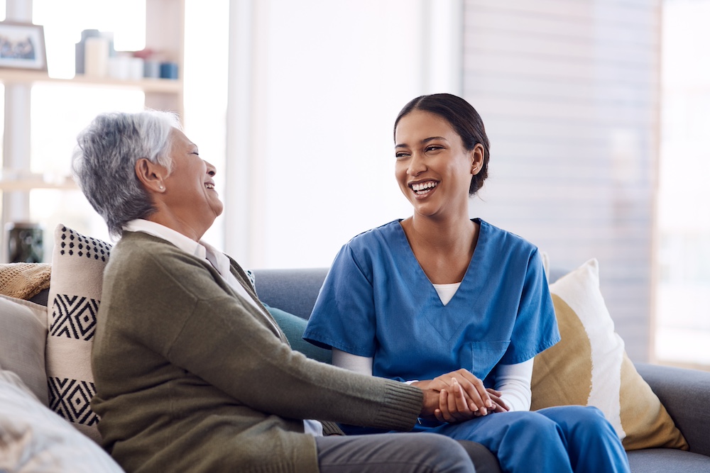 A smiling senior woman and her caregiver laugh and chat together