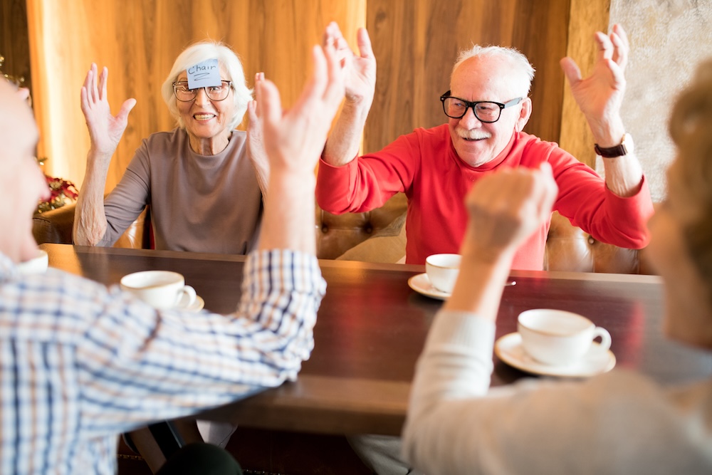 Group of senior friends at a senior living community playing a guessing game around a table.