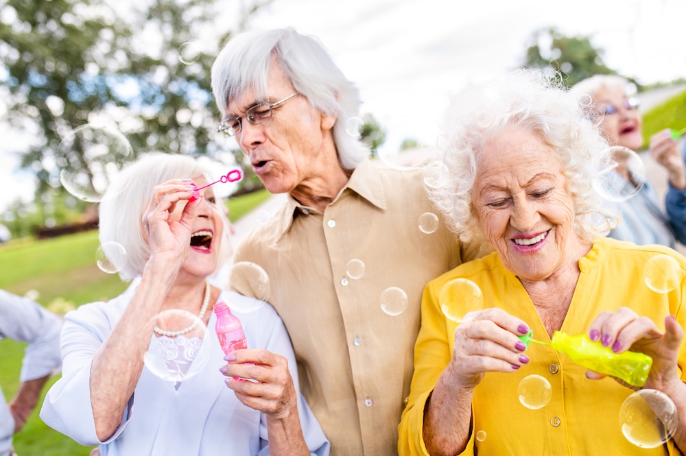 Group of senior friends outside blowing bubbles and enjoying the vibrant life at their Senior Assisted Living